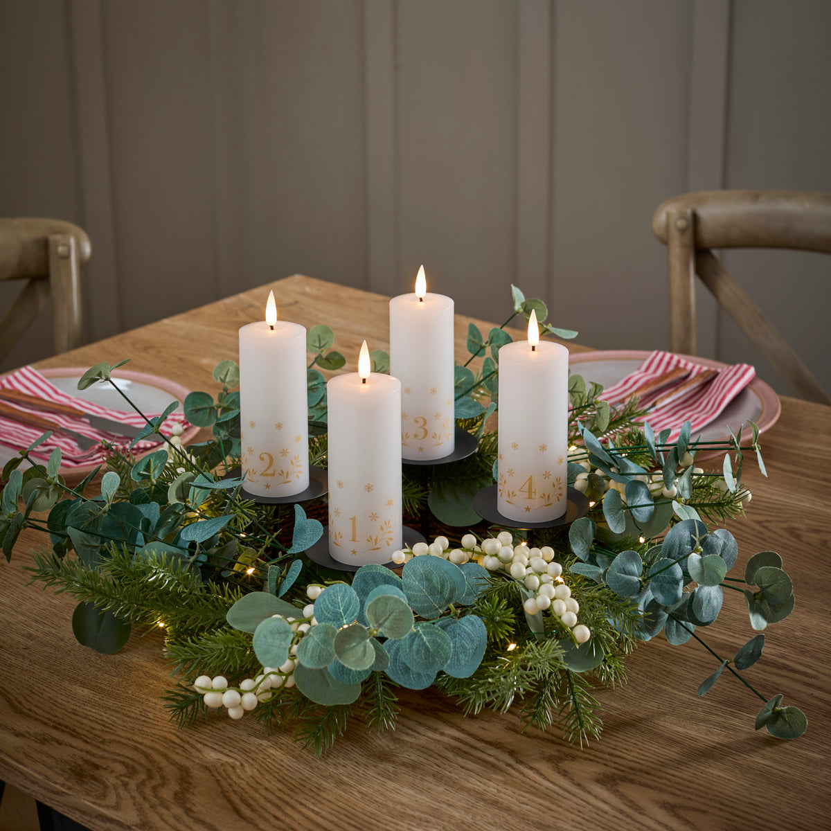 LED Adventskerzen mit Zahlen in einem Adventskranz aus Tannenzweigen und weißen Beeren auf Holztisch