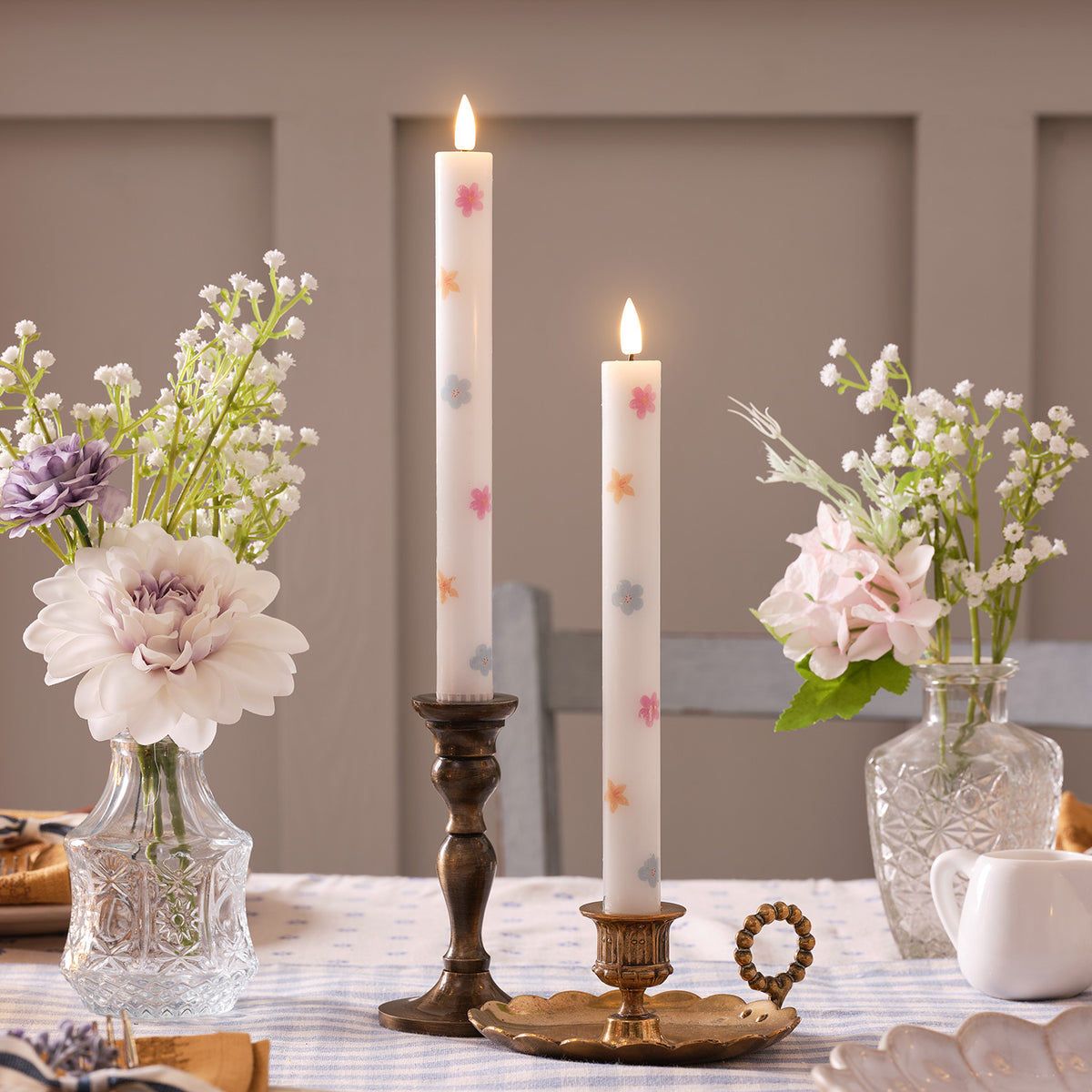 Zwei LED Stabkerzen mit Blumenmuster in Kerzenhaltern auf Tisch mit Blumen und Fernbedienung