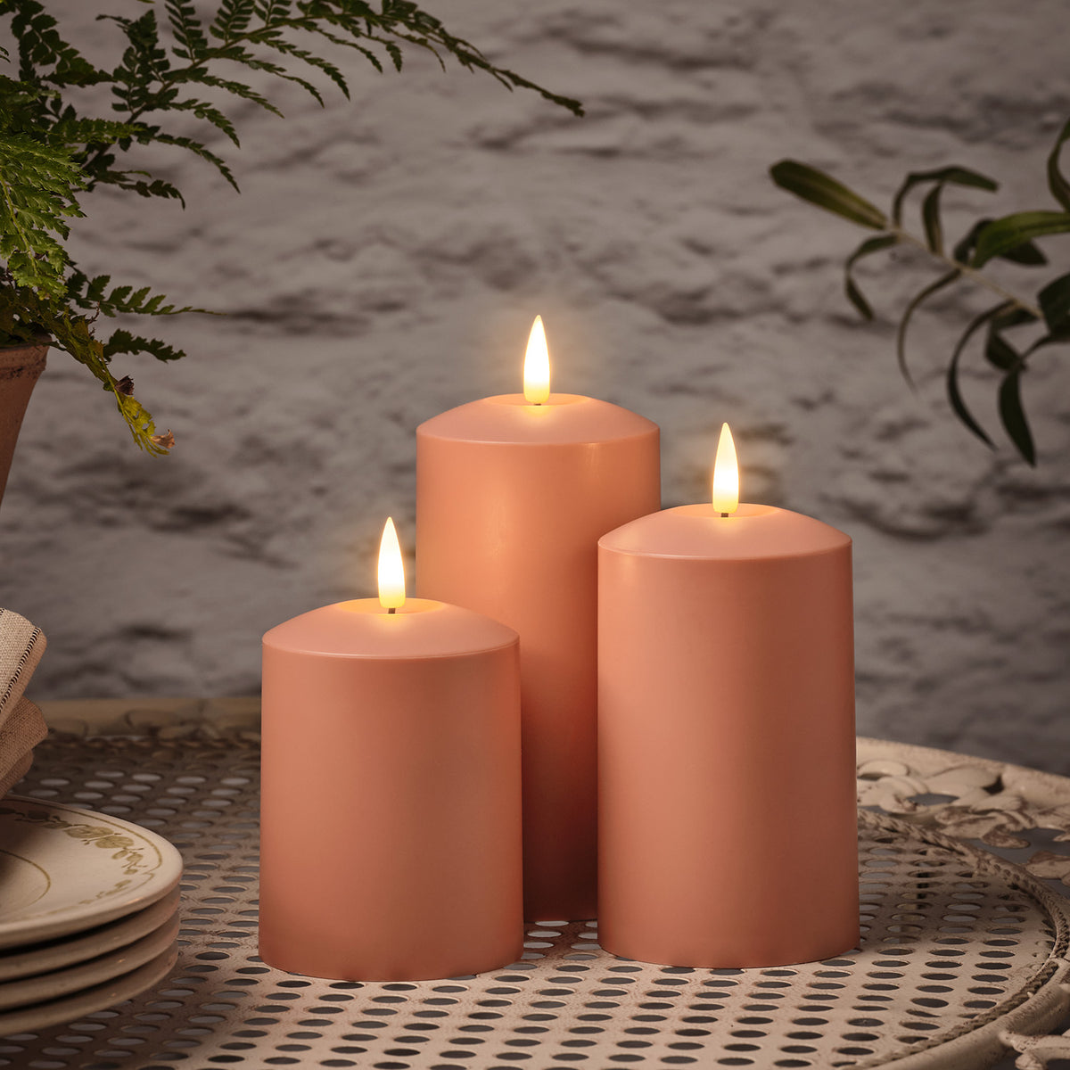 Trio aus terrakottafarbenen LED-Kerzen mit warmweißem Licht auf einem weißen Metalltisch