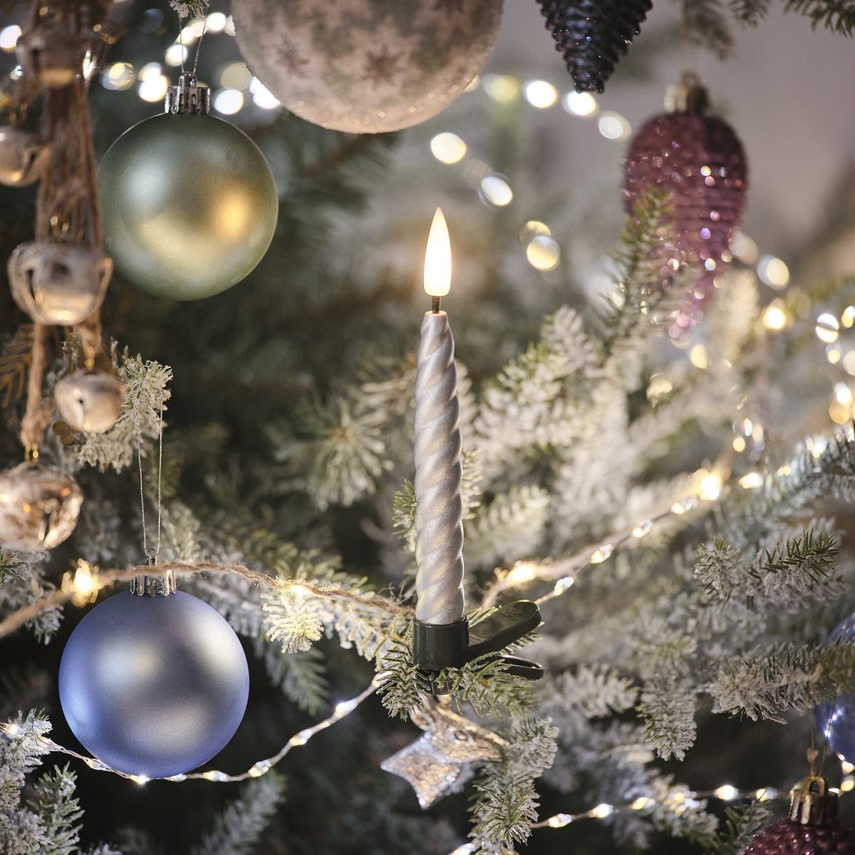 Silberne LED-Weihnachtsbaumkerze mit warmweiß flackernder Flamme an grünem Baumzweig