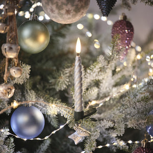 Silberne LED-Weihnachtsbaumkerze mit warmweiß flackernder Flamme an grünem Baumzweig