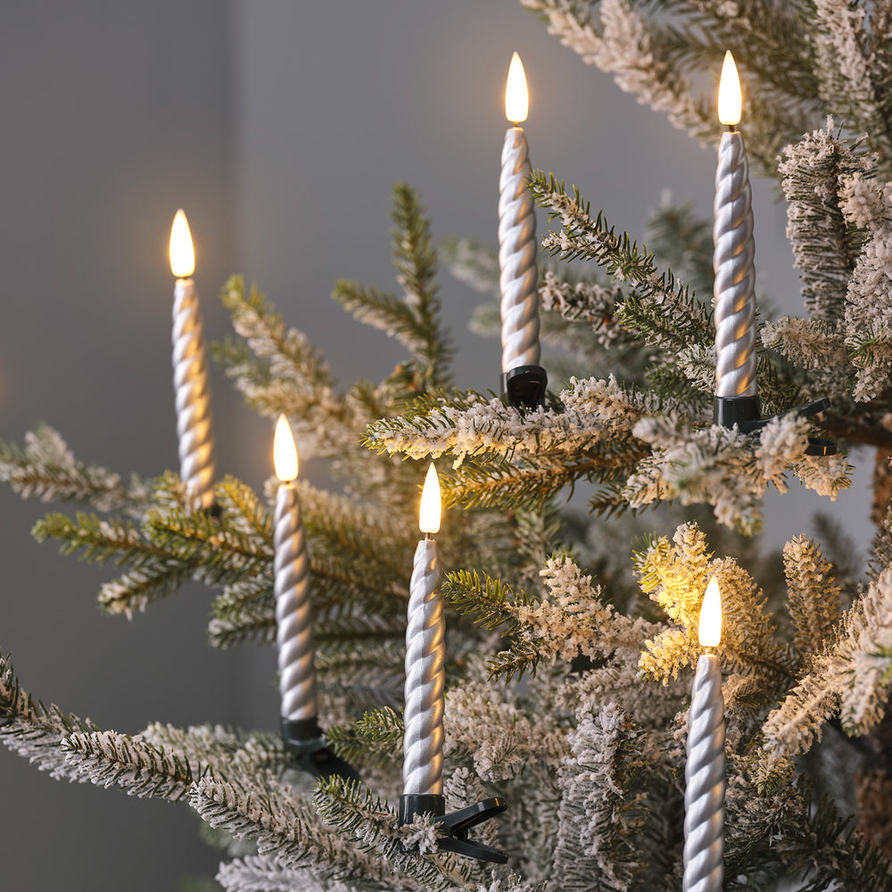 Mehrere silberne LED-Weihnachtsbaumkerzen mit Clips an verschneiten Tannenzweigen befestigt