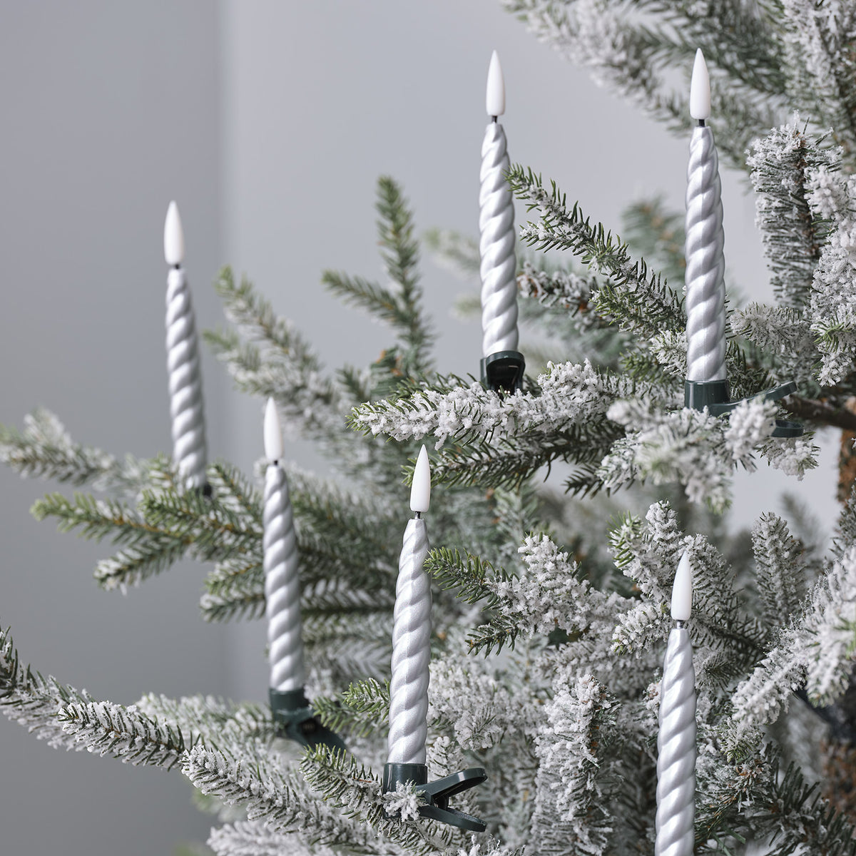Silberne LED-Weihnachtsbaumkerzen mit Clips an verschneiten Tannenzweigen in Nahaufnahme