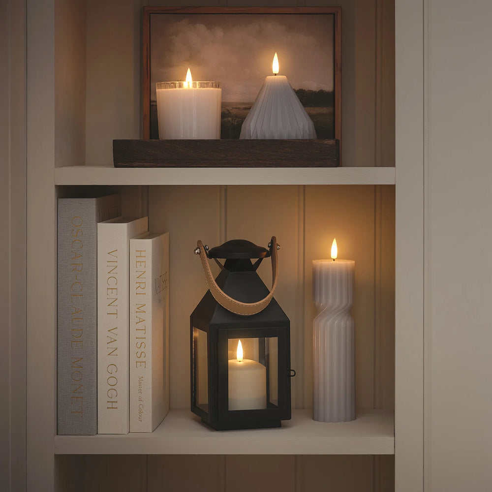 Regal mit LED-Kerzen, Laterne und Büchern in warmem Licht dekoriert