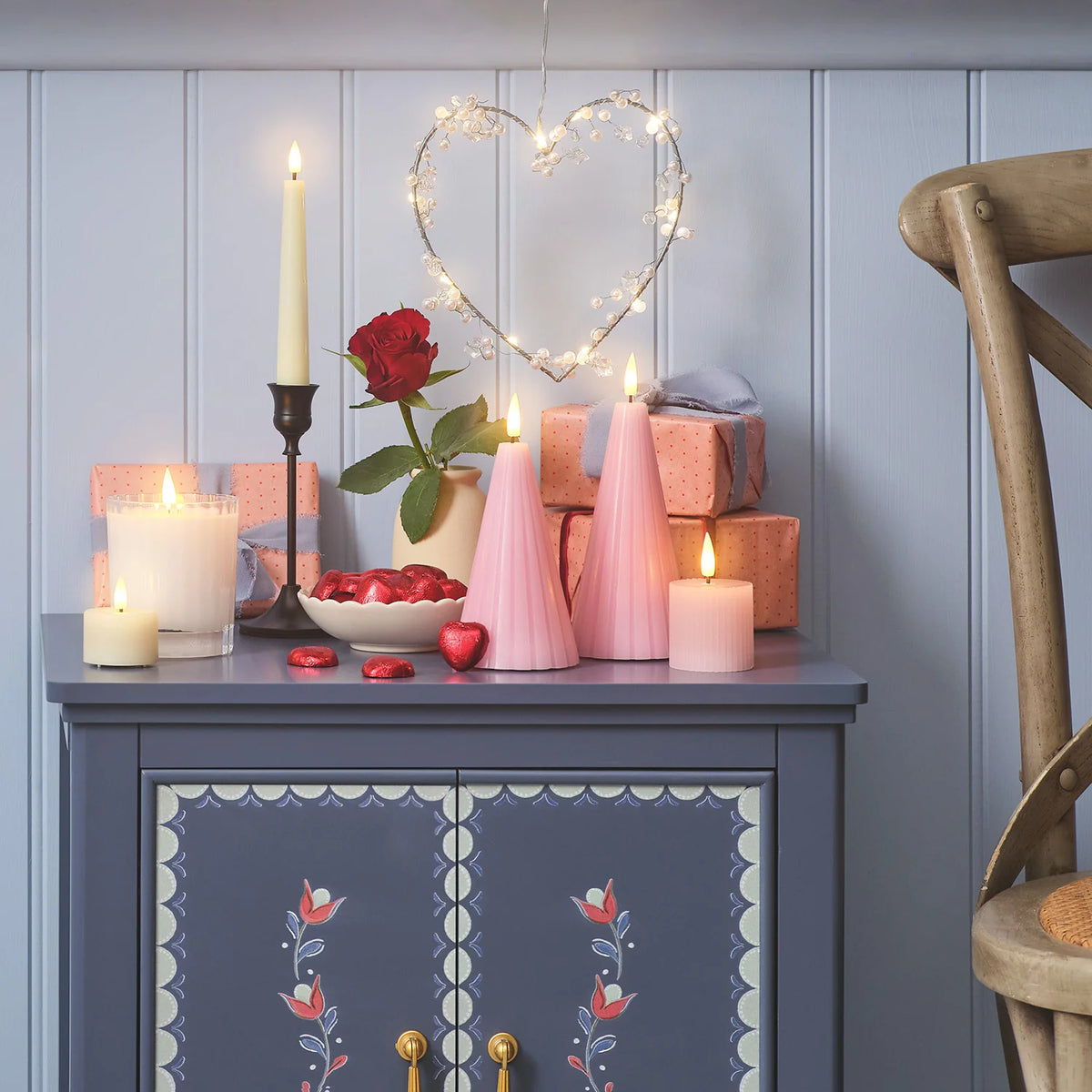 LED-Kegelkerzen in Blush Pink auf Kommode mit Kerzen, Rosen und Herz-Lichterkette