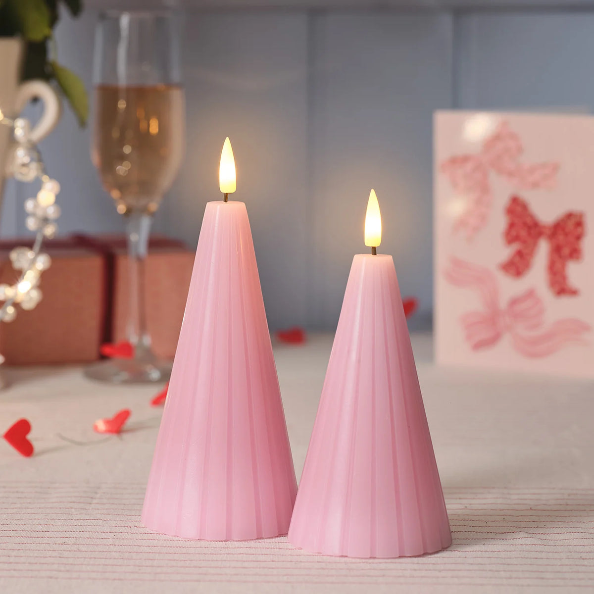 Zwei rosa LED-Kegelkerzen mit warmweiß flackernder Flamme vor Valentinstagsdeko