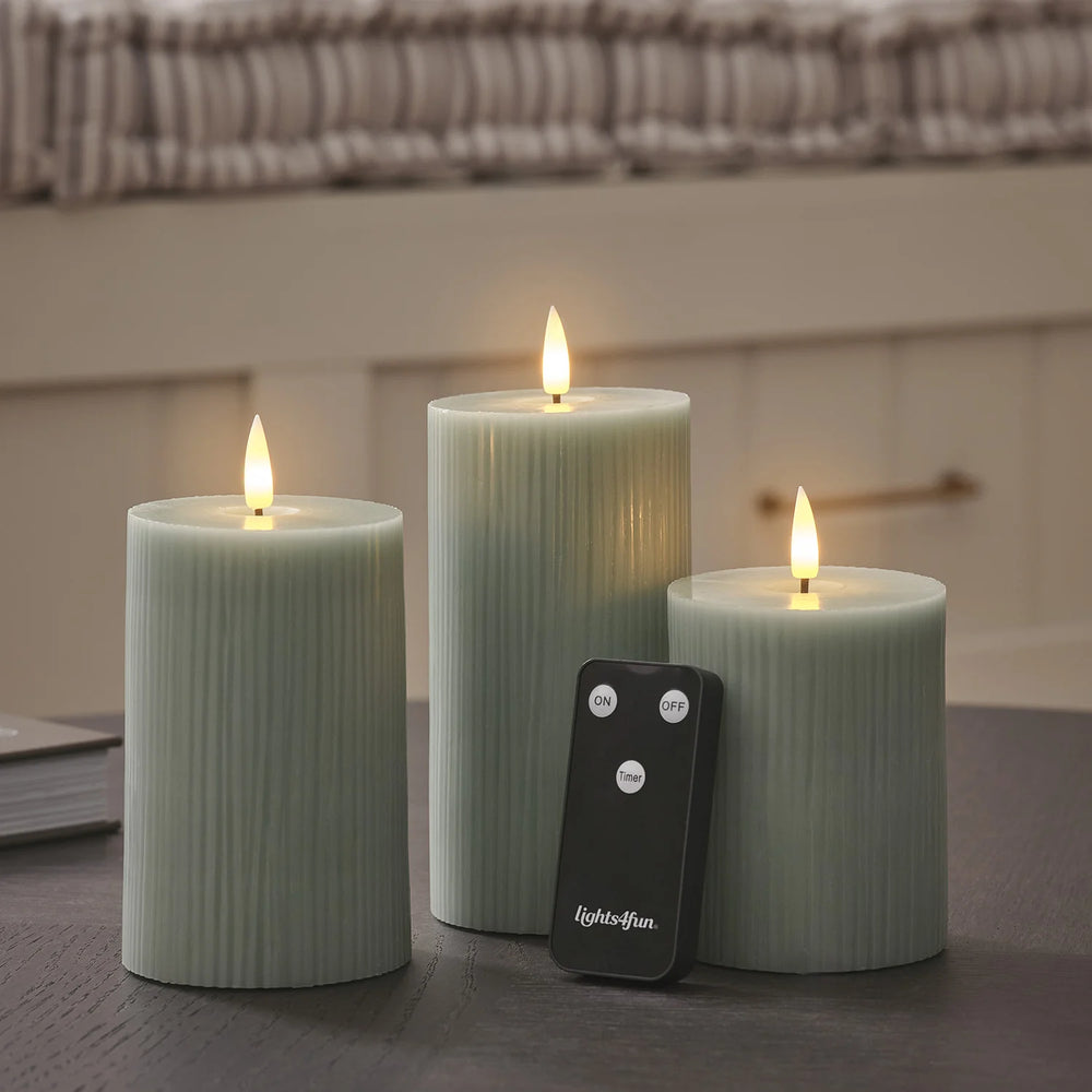 LED-Stumpenkerzen in Salbeigrün mit Fernbedienung auf dunklem Tisch