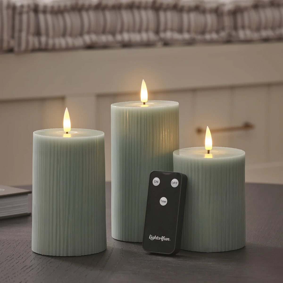 LED-Stumpenkerzen in Salbeigrün mit Fernbedienung auf dunklem Tisch