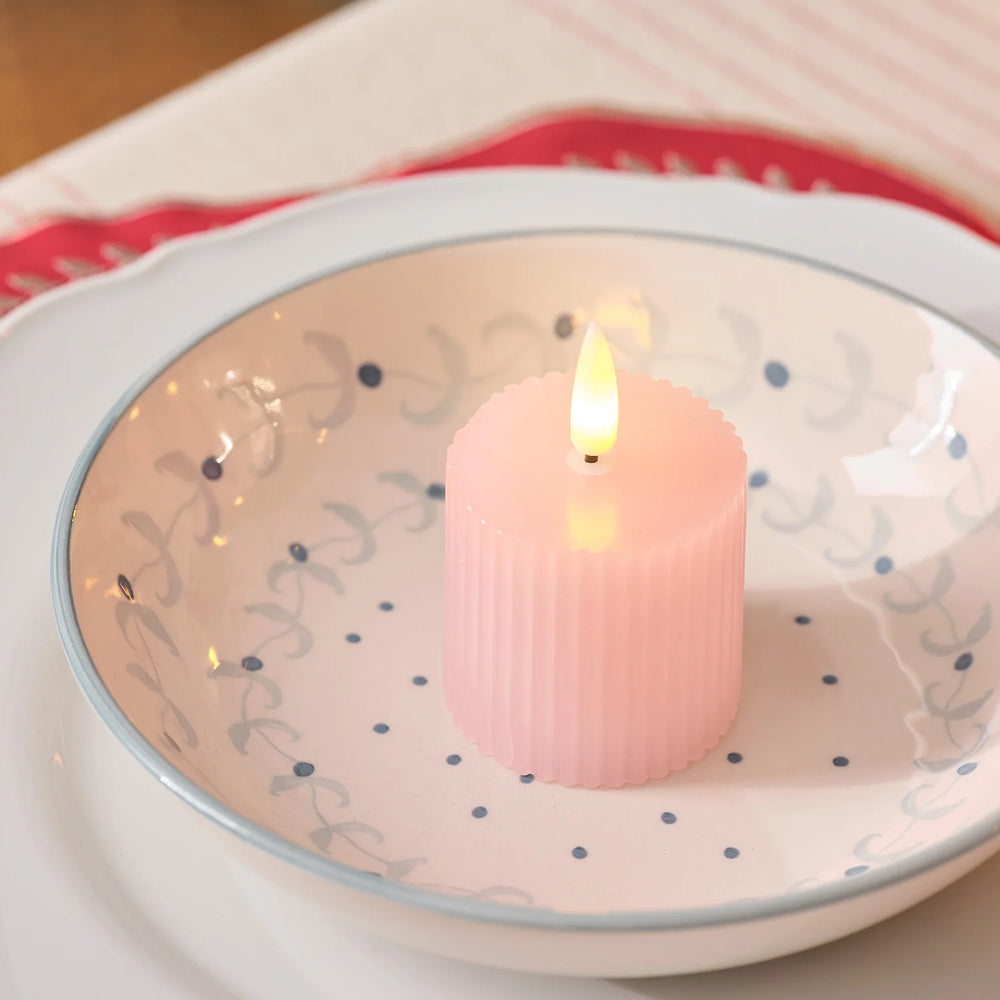 Nahaufnahme einer rosa geriffelten LED-Votivkerze mit flackernder Flamme auf einem gemusterten Teller