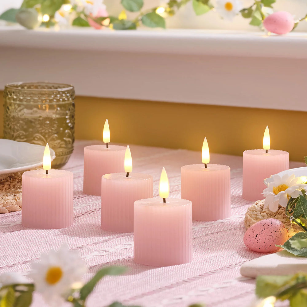 Sechs rosa geriffelte LED-Votivkerzen mit warmweiß flackernden Flammen auf einem Tisch dekoriert
