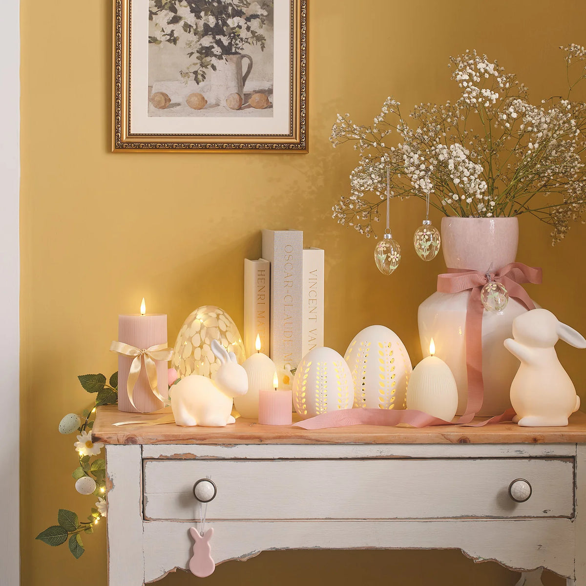 Osterdeko mit LED-Eierkerzen, Kerzen, Hasenfigur und Blumen auf weißem Sideboard