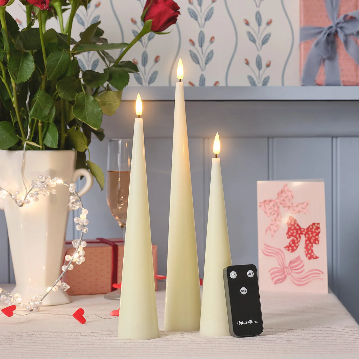 TruGlow LED-Kerzen in Kegelform mit Fernbedienung auf Tisch mit Herz-Lichterkette und Geschenkboxen