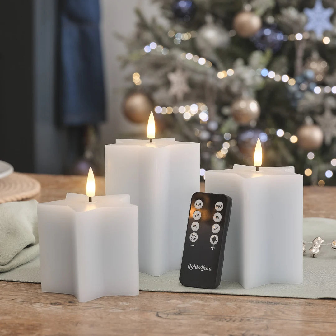 Weiße LED-Kerzen mit Fernbedienung (lights4fun-Branding) auf Leinen-Tischdecke, warmweiße brennende Flammen, Weihnachtsbaum bokeh Beleuchtung im Hintergrund.