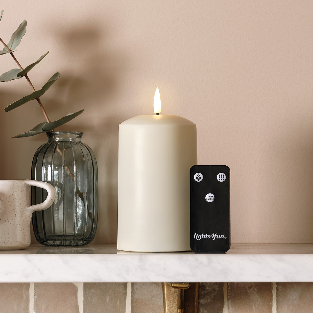 TruGlow AIR LED-Kerze mit Fernbedienung neben Glasvase und Tasse auf Regal