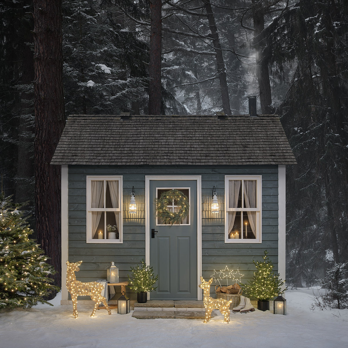Winterliches Haus mit blau gestrichener Tür, LED-Weihnachtskranz und beleuchteten Rentierfiguren