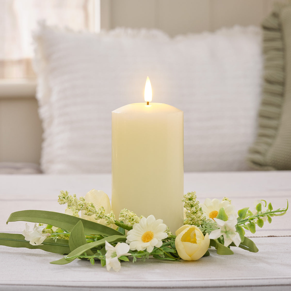 Kerzenring mit Frühlingsblumen um eine brennende cremefarbene Stumpenkerze