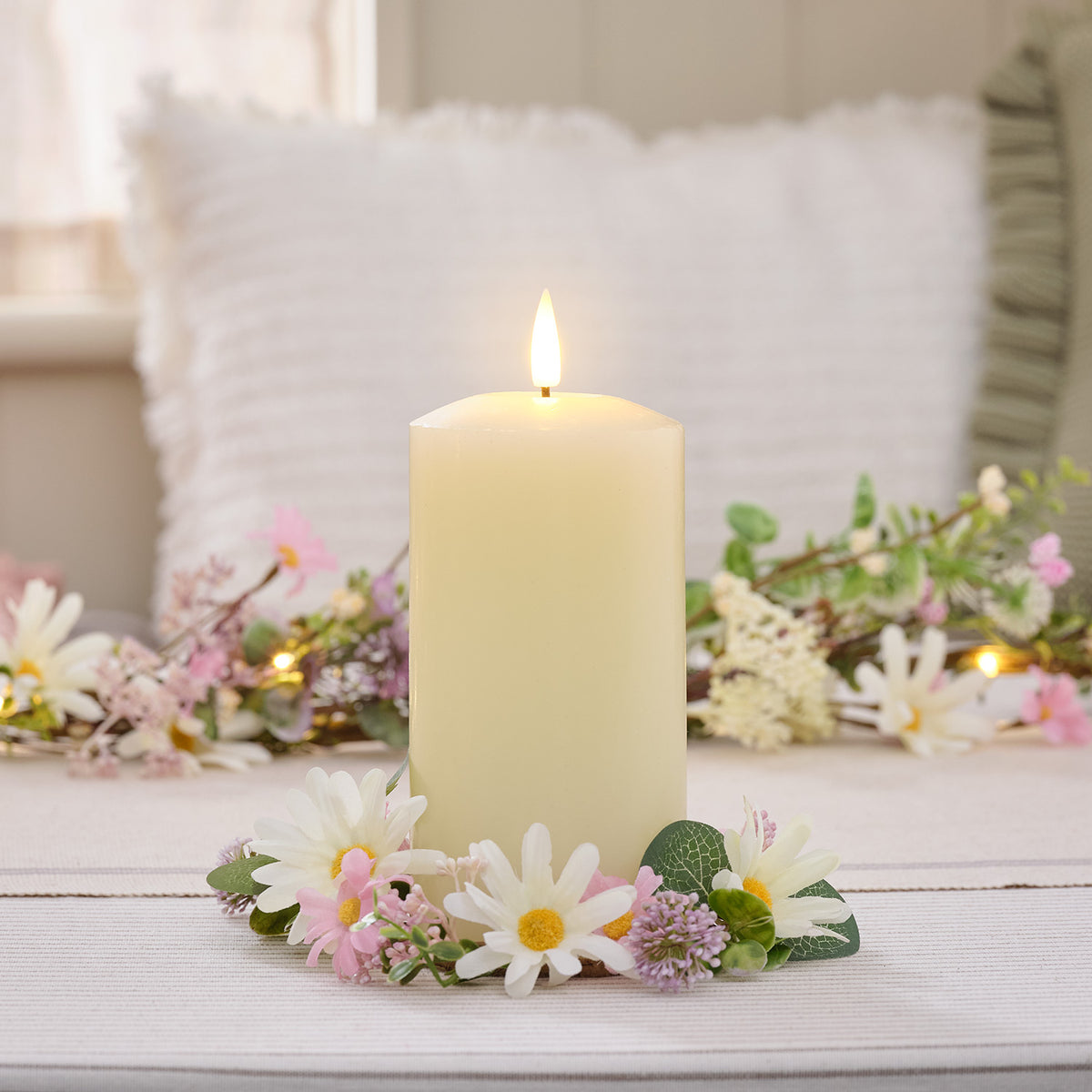Brennende LED-Stumpenkerze umgeben von Frühlings-Kerzenring mit Gänseblümchen und Wildblumen auf Tisch