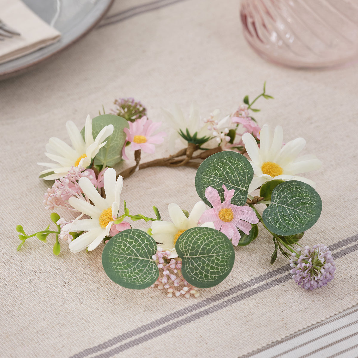 Kerzenring mit weißen Gänseblümchen, rosa Blüten und grünen Blättern auf Stoff mit Streifenmuster