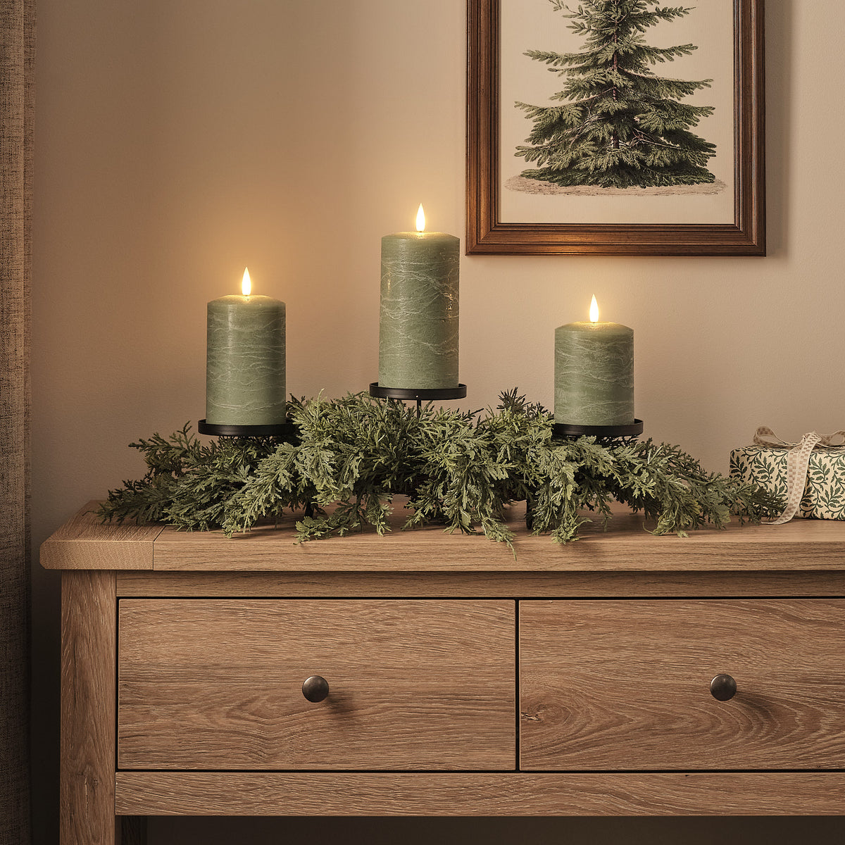 Weihnachtsgesteck mit drei grünen LED-Stumpenkerzen auf einem Holztisch vor Wandbild Tanne