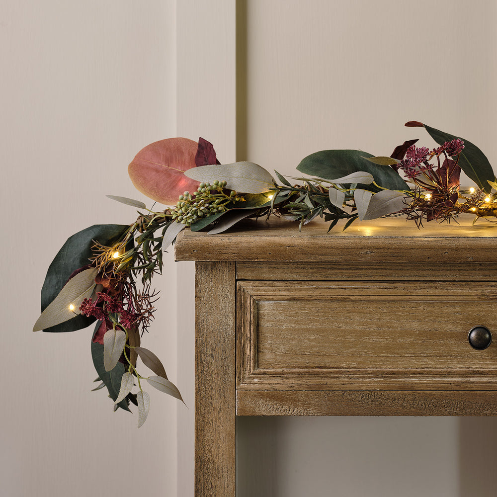 Herbstliche Girlande mit grünen und roten Blättern und warm leuchtender Micro LED Lichterkette auf Holztisch