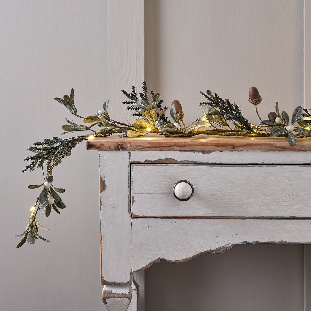 Weihnachtsgirlande mit Eicheln, weißen Beeren und Micro-LED-Lichterkette auf weißem Holztisch