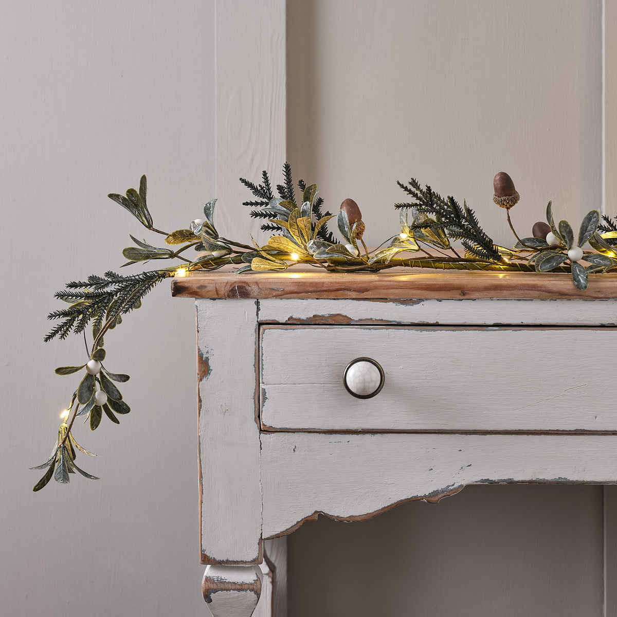 Weihnachtsgirlande mit Eicheln, weißen Beeren und Micro-LED-Lichterkette auf weißem Holztisch