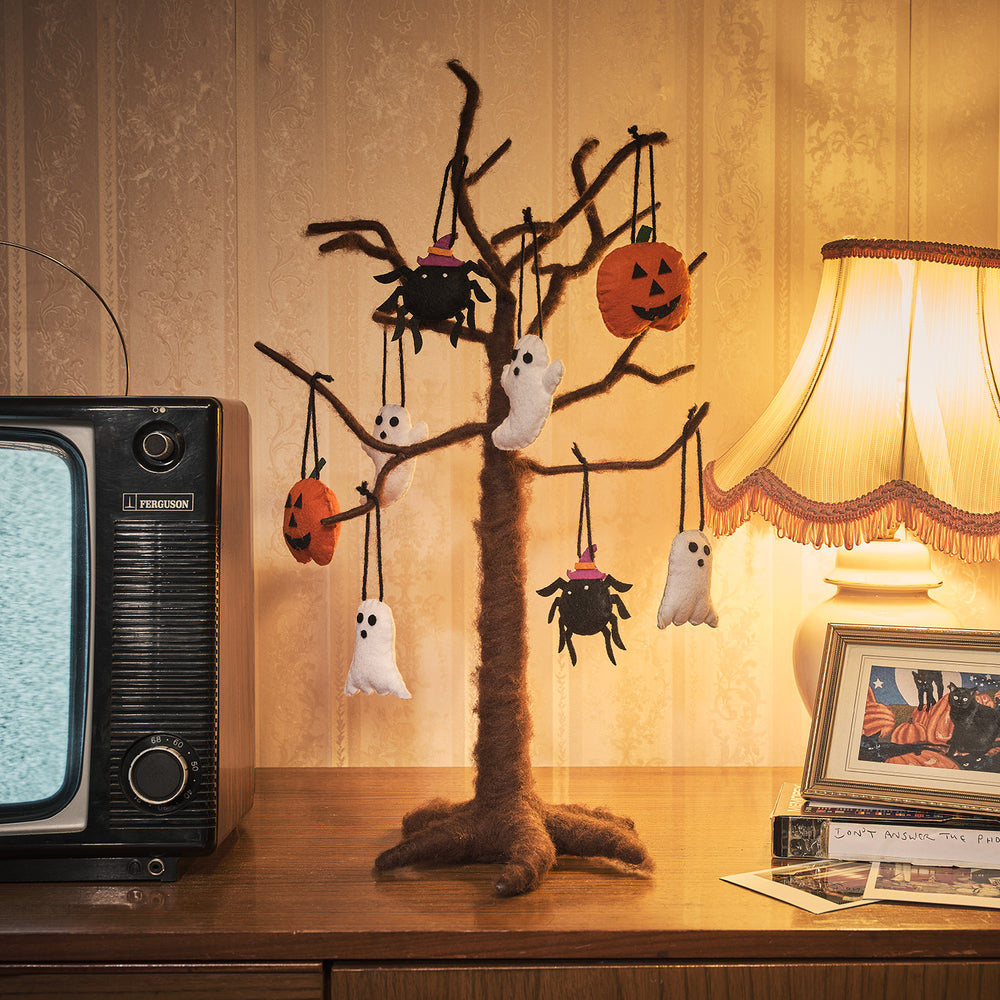 Brauner Filzbaum mit Halloween-Filzanhängern Kürbis, Geist und Spinne auf Holzkommode neben Lampe
