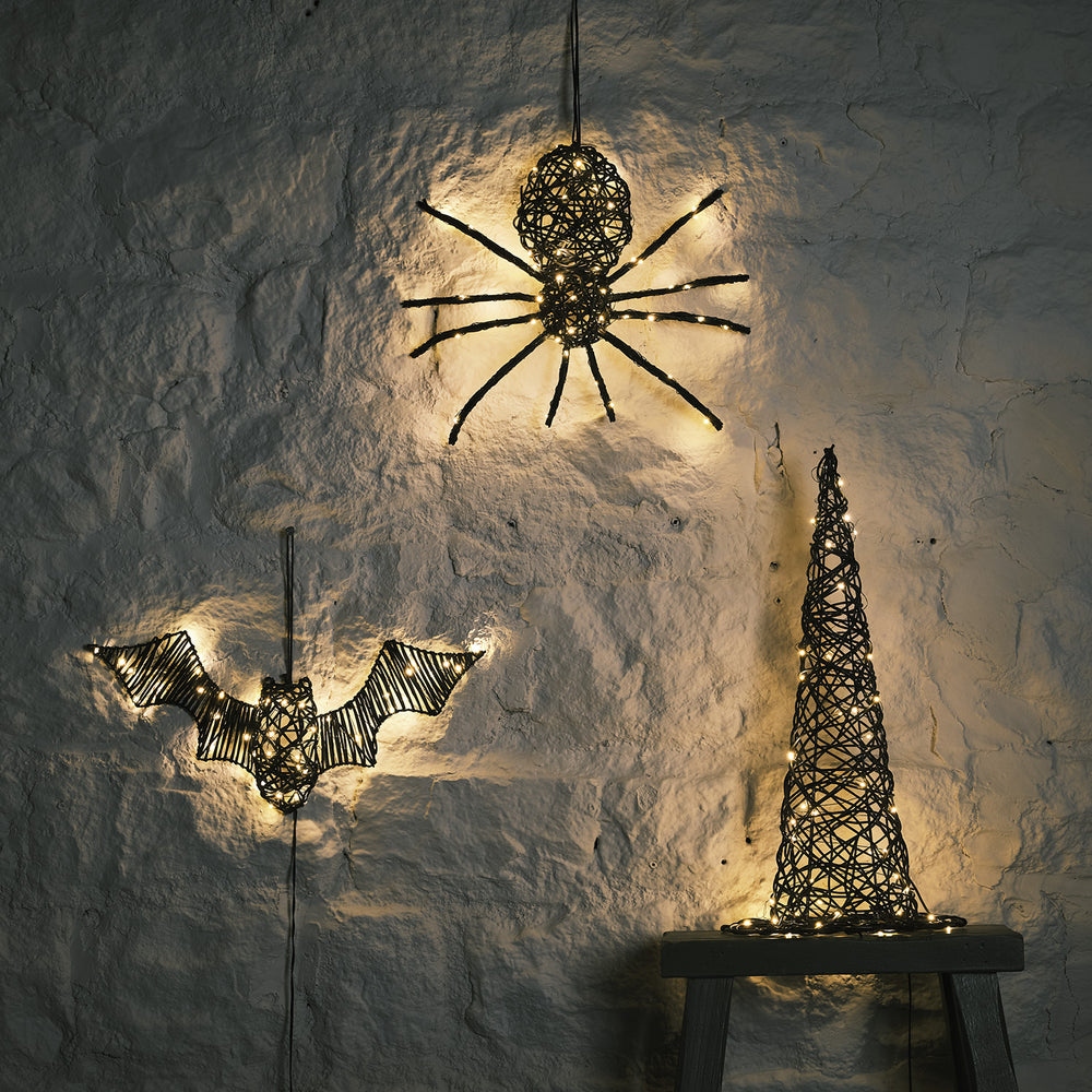 LED beleuchtete Rattan-Spinne, Fledermaus und Hexenhut an weißer Wand im Dunkeln
