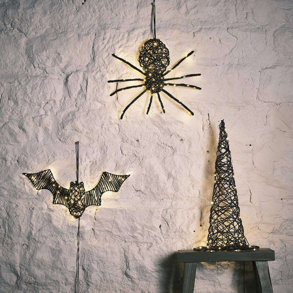 LED beleuchtete Rattan-Spinne, Fledermaus und Hexenhut an weißer Wand bei Tageslicht