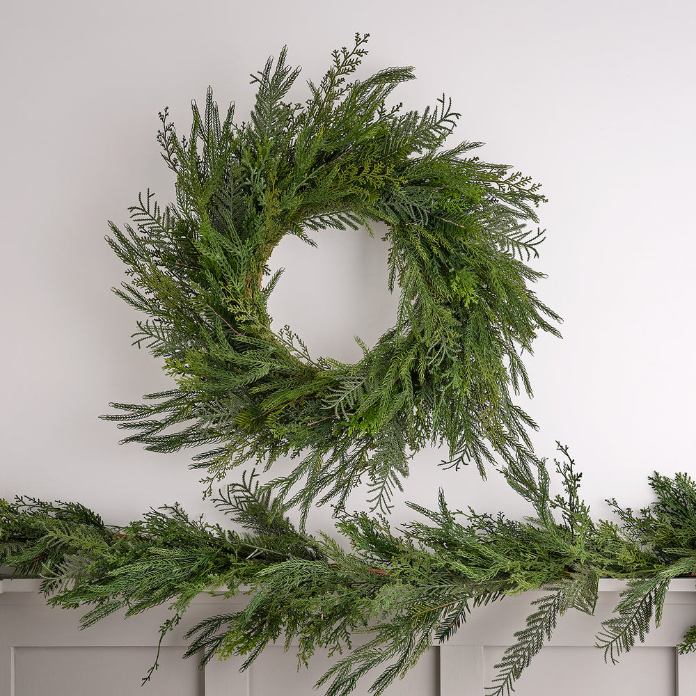 Weihnachtskranz aus künstlichem Zypressen-Nadelwerk an weißer Wand