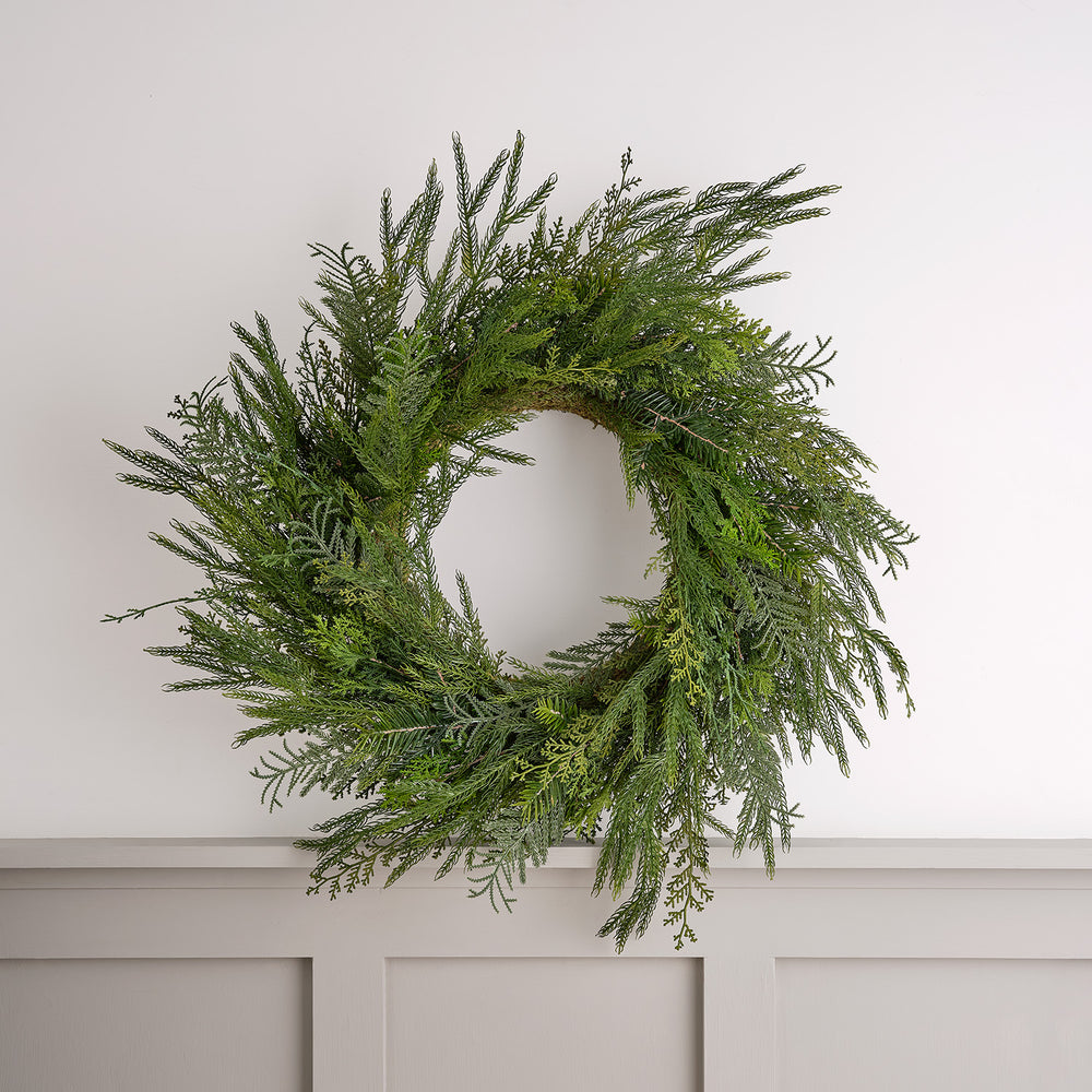 Dichter Weihnachtskranz aus künstlichen Zypressenzweigen an weißer Wand