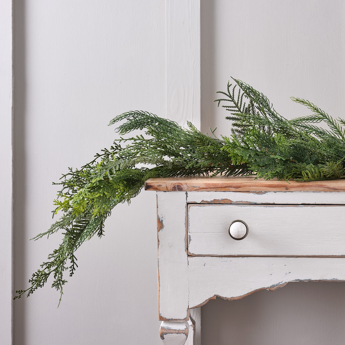 Weihnachtsgirlande aus künstlichen Zypressenzweigen auf weißem Holztisch