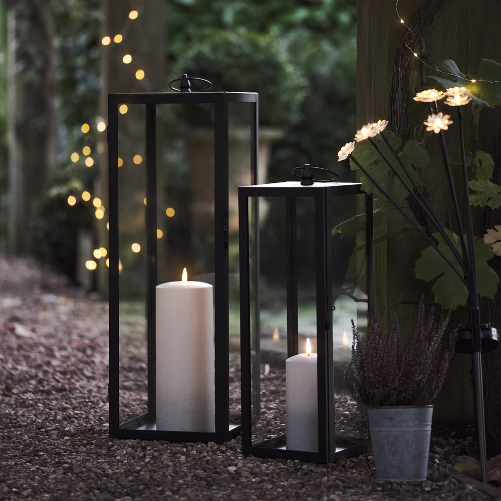 Zwei schwarze Gartenlaternen mit TruGlow® LED-Kerzen auf Kiesboden im Außenbereich bei Dämmerung