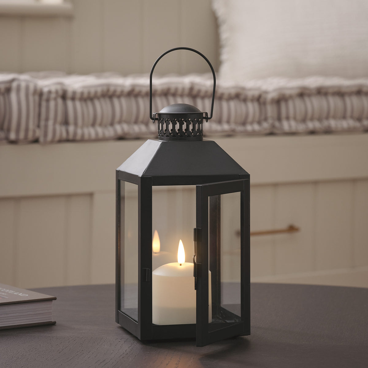 Schwarze Laterne mit geöffneter Tür und TruGlow LED-Kerze auf dunklem Tisch