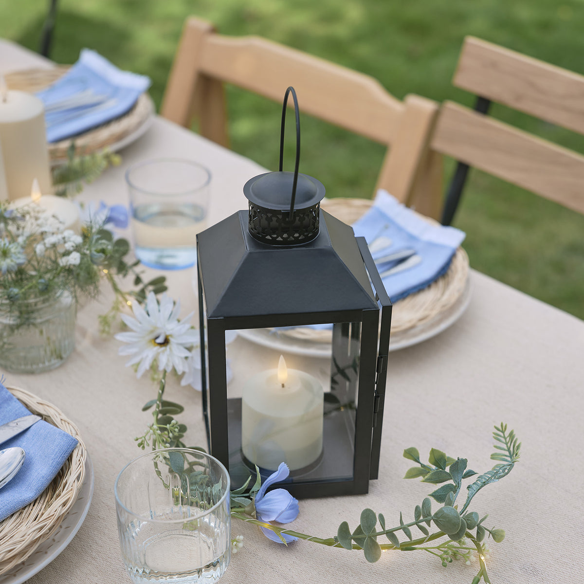 Schwarze Laterne mit TruGlow LED-Kerze auf gedecktem Gartentisch mit Blumen und Gläsern
