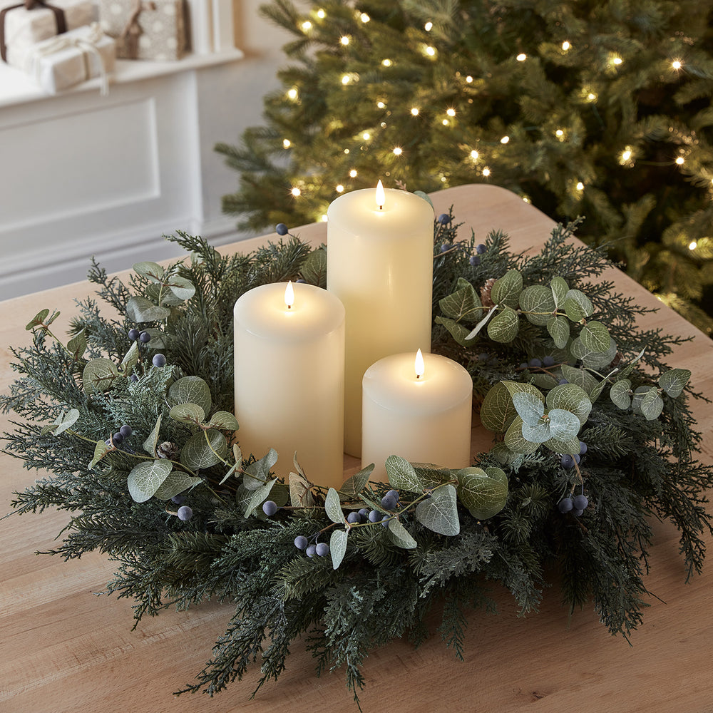 Nahaufnahme eines Weihnachtskranzes mit künstlichen Blättern, Beeren und drei elfenbeinfarbenen LED Kerzen