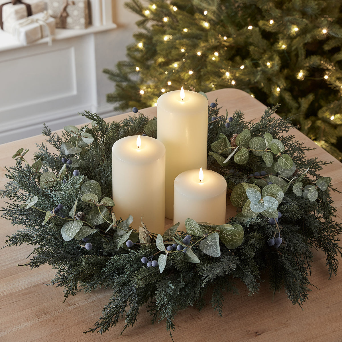 Nahaufnahme eines Weihnachtskranzes mit künstlichen Blättern, Beeren und drei elfenbeinfarbenen LED Kerzen