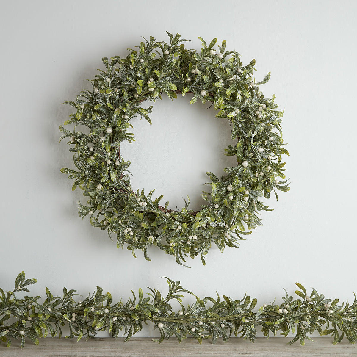 Weihnachtskranz und Girlande aus künstlichem Mistelzweig mit weißen Beeren ohne Beleuchtung an Wand
