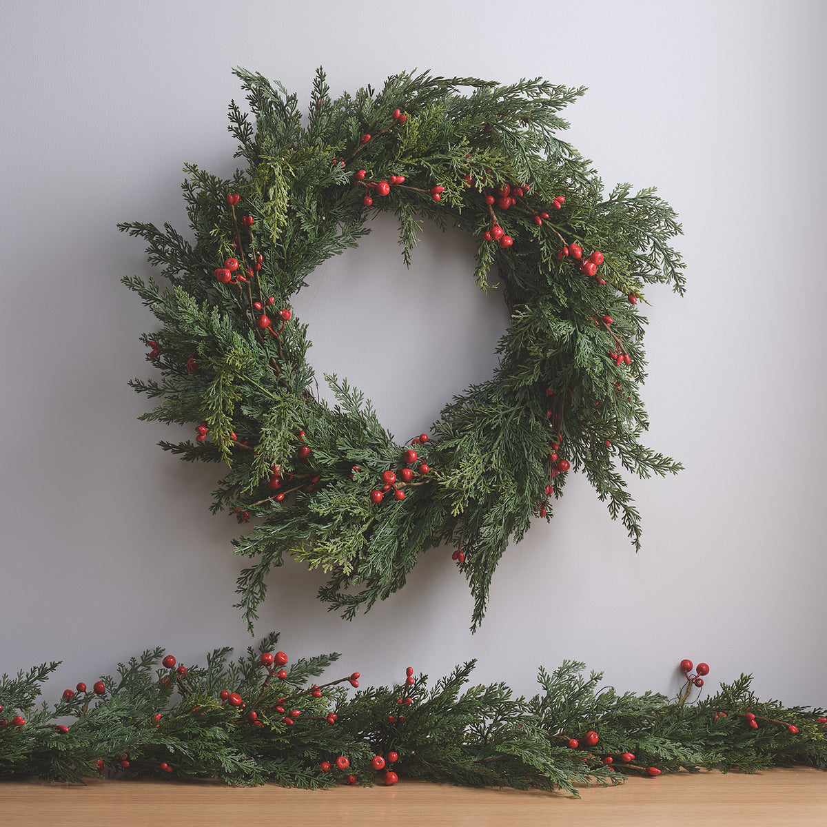 Weihnachtskranz mit roten Beeren ohne Beleuchtung an weißer Wand mit Tannenzweigen