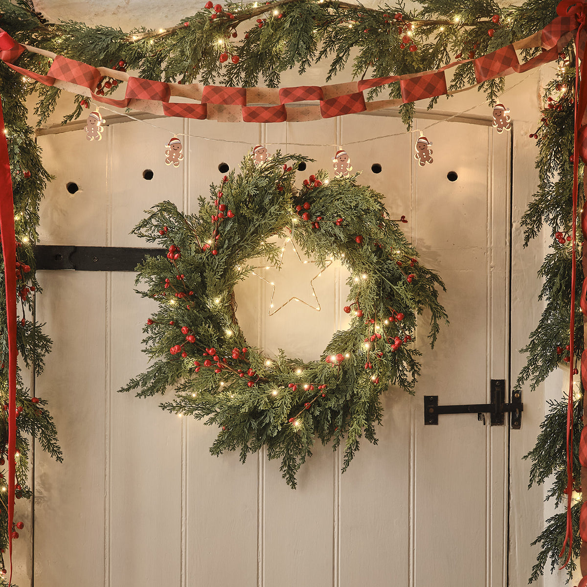 Beleuchteter Weihnachtskranz mit roten Beeren und Stern aus Lichterkette an Holztür