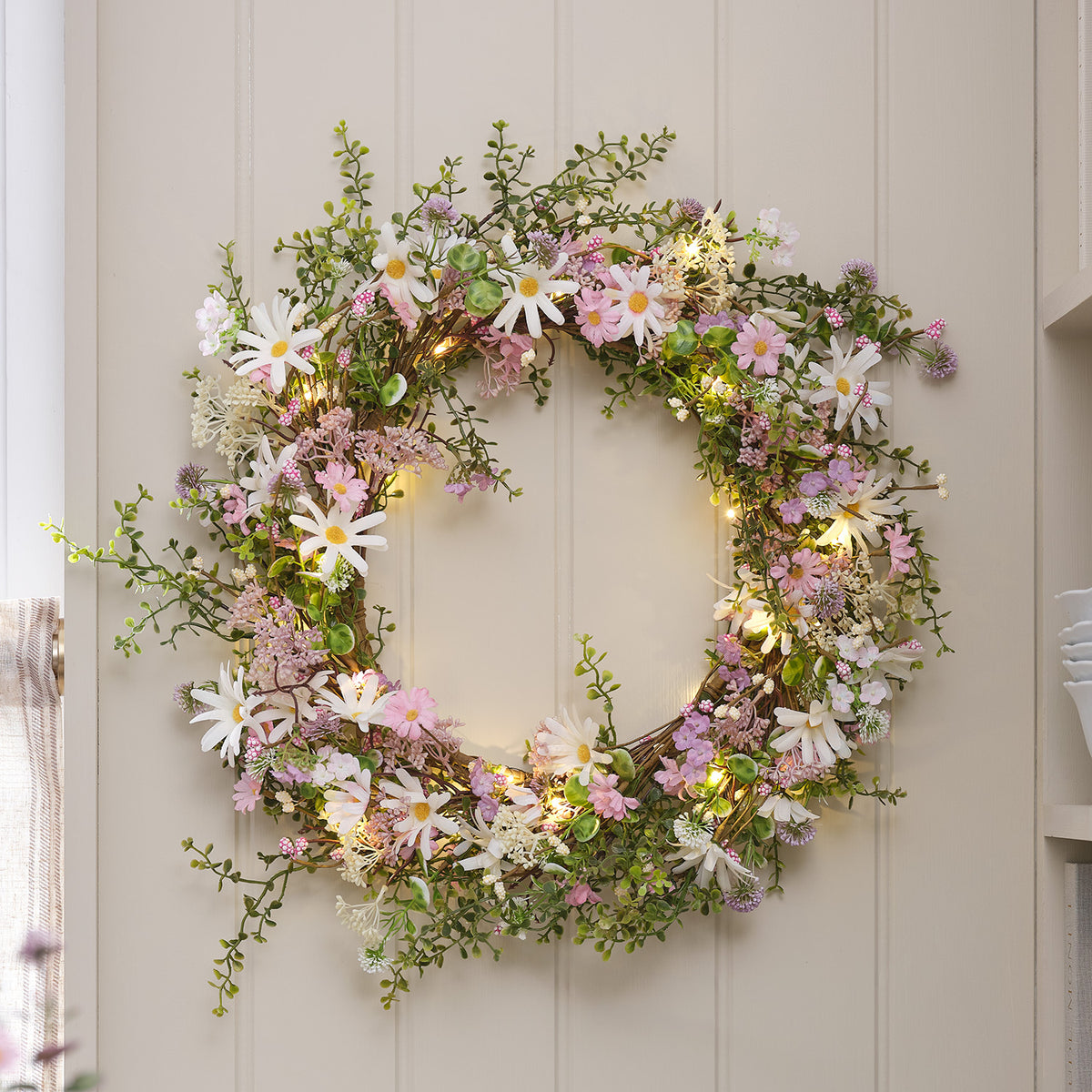 Nahaufnahme LED-Blumenkranz mit zarten weißen und rosa Margeriten und grünen Blättern