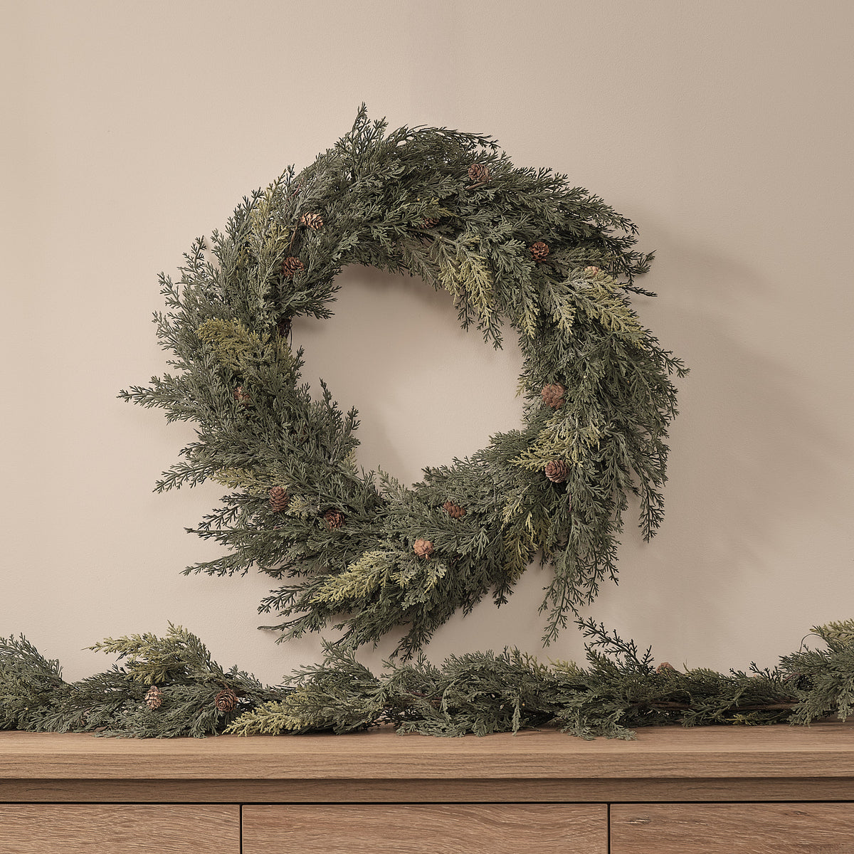Weihnachtskranz mit Tannenzapfen und warmweißen LEDs auf hellen Wandhintergrund