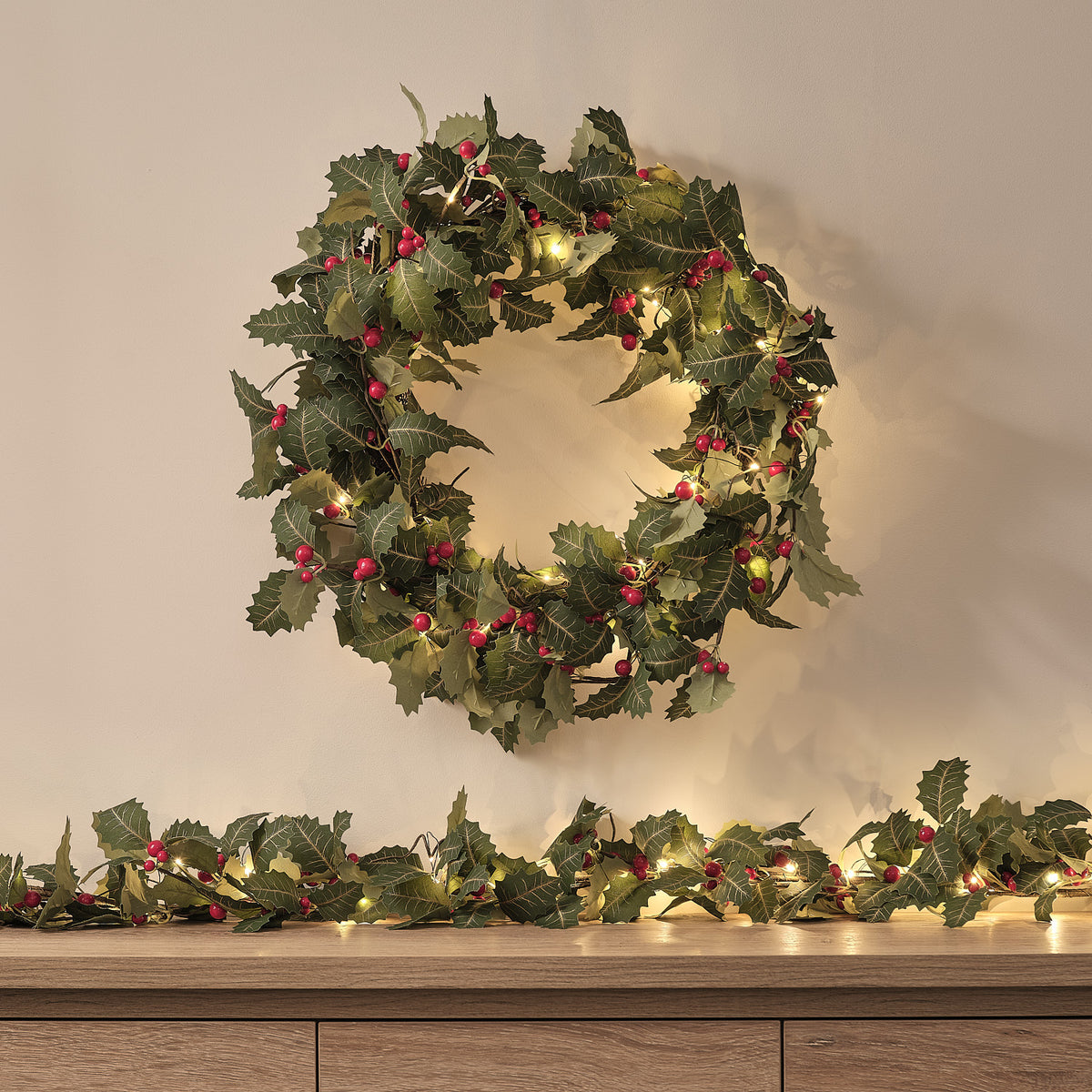 LED-Türkranz mit Stechpalmenblättern, roten Beeren und warmweißen LEDs über Sideboard