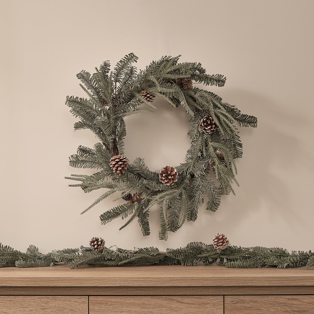 Unbeleuchteter Weihnachtskranz aus Kunstgrün mit Zapfen an heller Wand