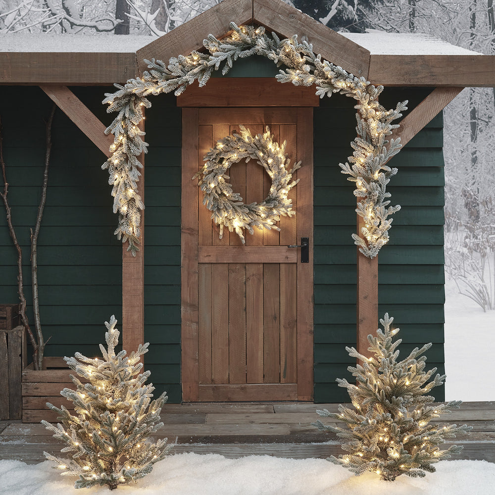 Verschneiter Weihnachtskranz und Girlande mit warmweißen LEDs an Holztür und Eingang