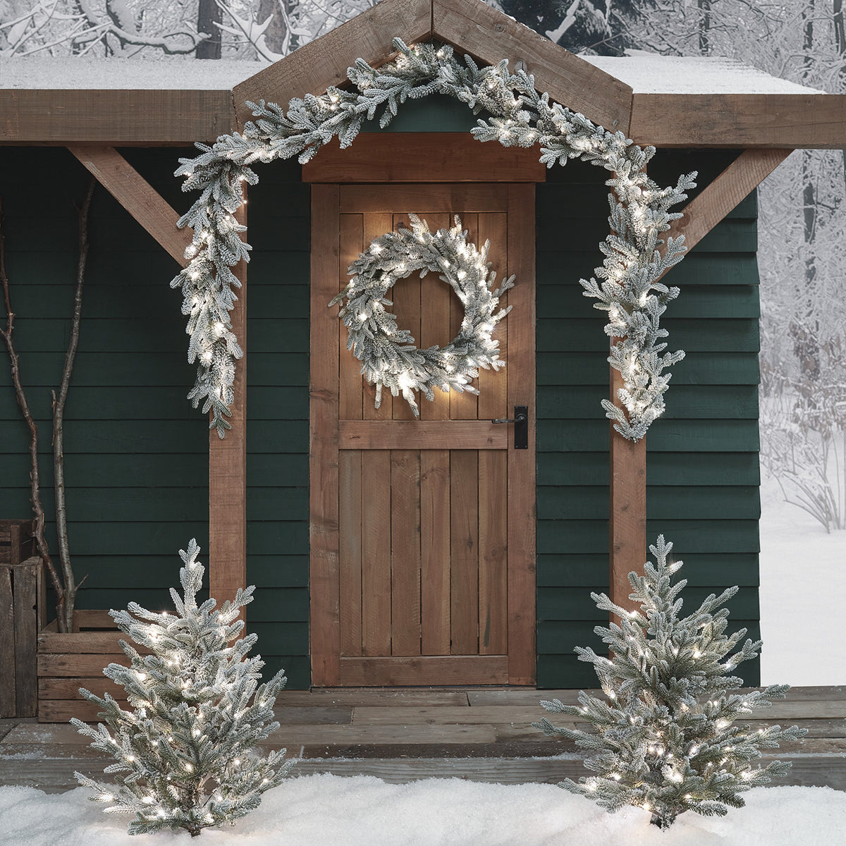 Verschneiter Weihnachtskranz und Girlande mit weißen LEDs an Holztür und Eingang