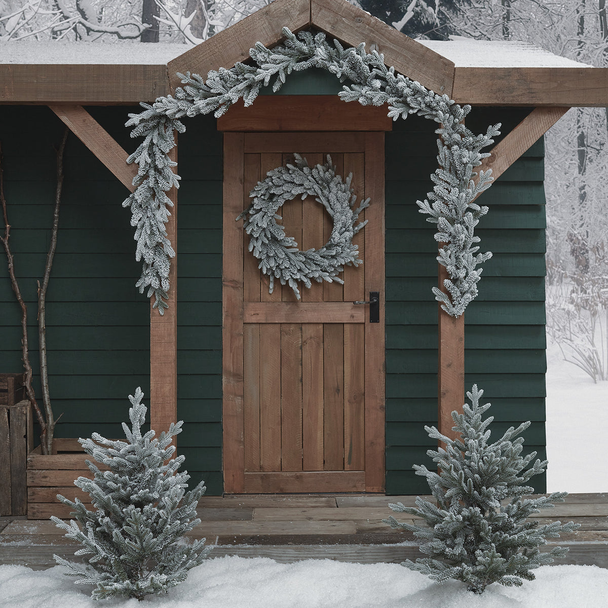 Verschneiter Weihnachtskranz und Girlande ohne Beleuchtung an Holztür und Eingang