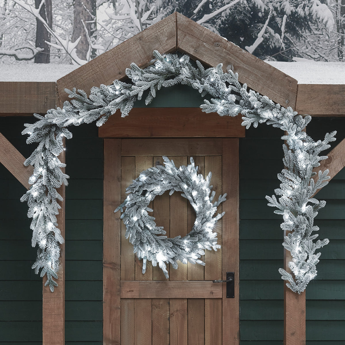 Verschneite Weihnachtsgirlande und Kranz mit kaltweißen LEDs an Holztür und Dachgiebel