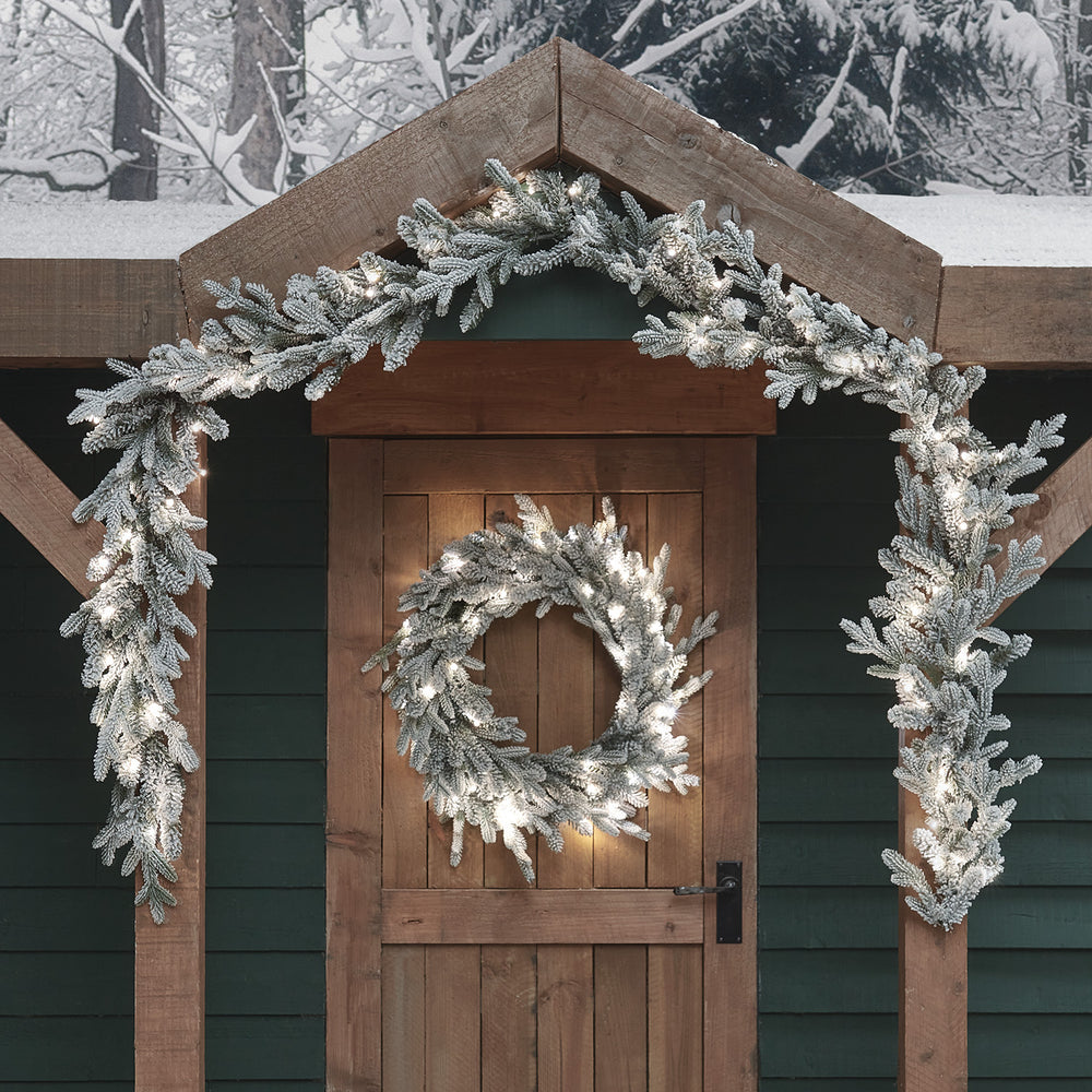 Weihnachtsgirlande und Kranz mit weißen LEDs beleuchtet an Holztür und Dachgiebel
