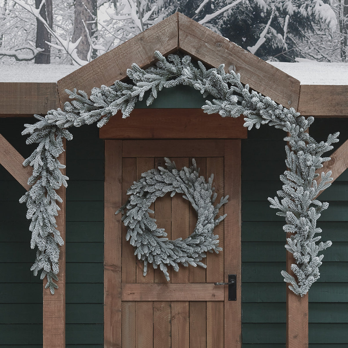 Verschneite Weihnachtsgirlande und Kranz ohne Beleuchtung an Holztür und Dachgiebel